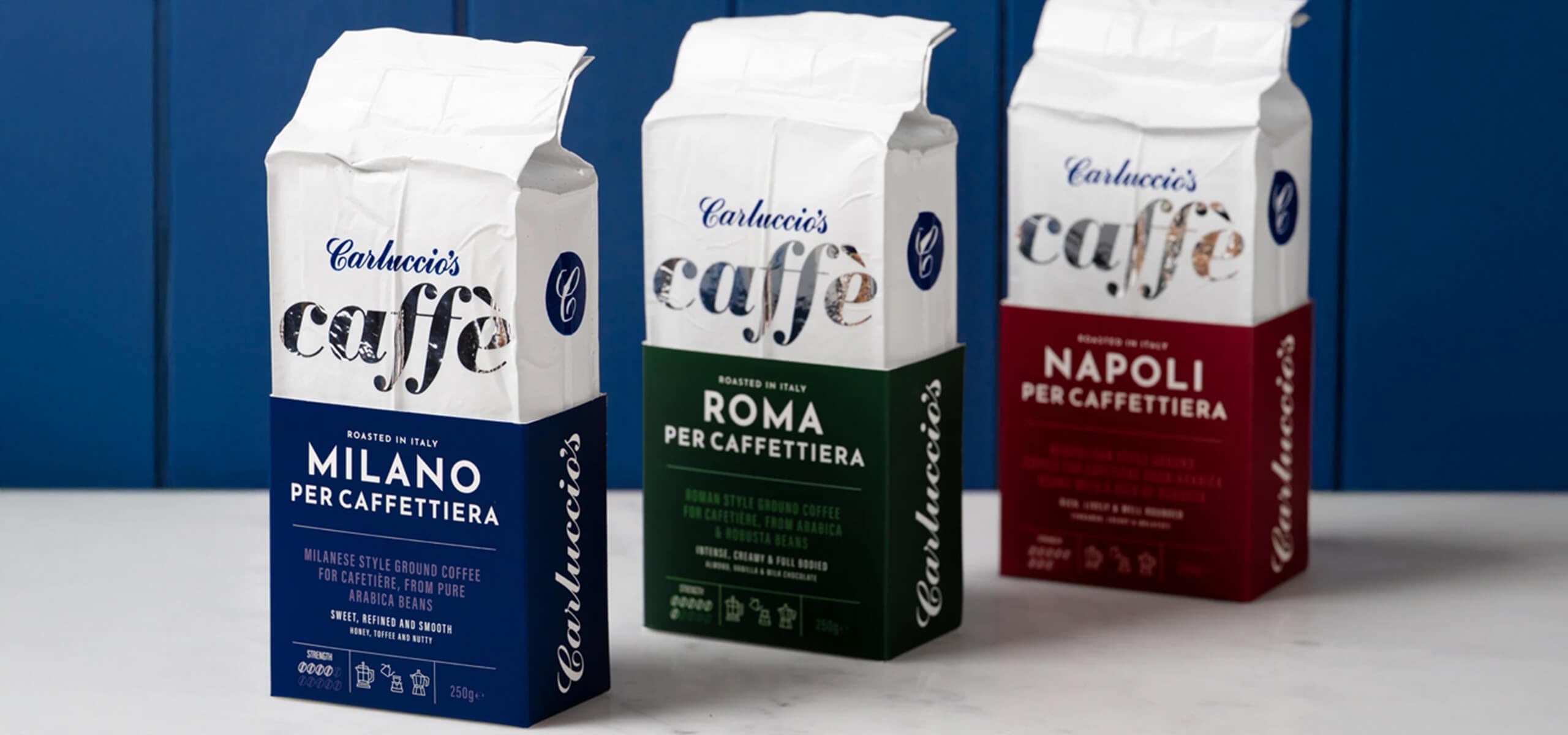 Three Carluccio's caffe coffee packaging on a white surface with a blue background