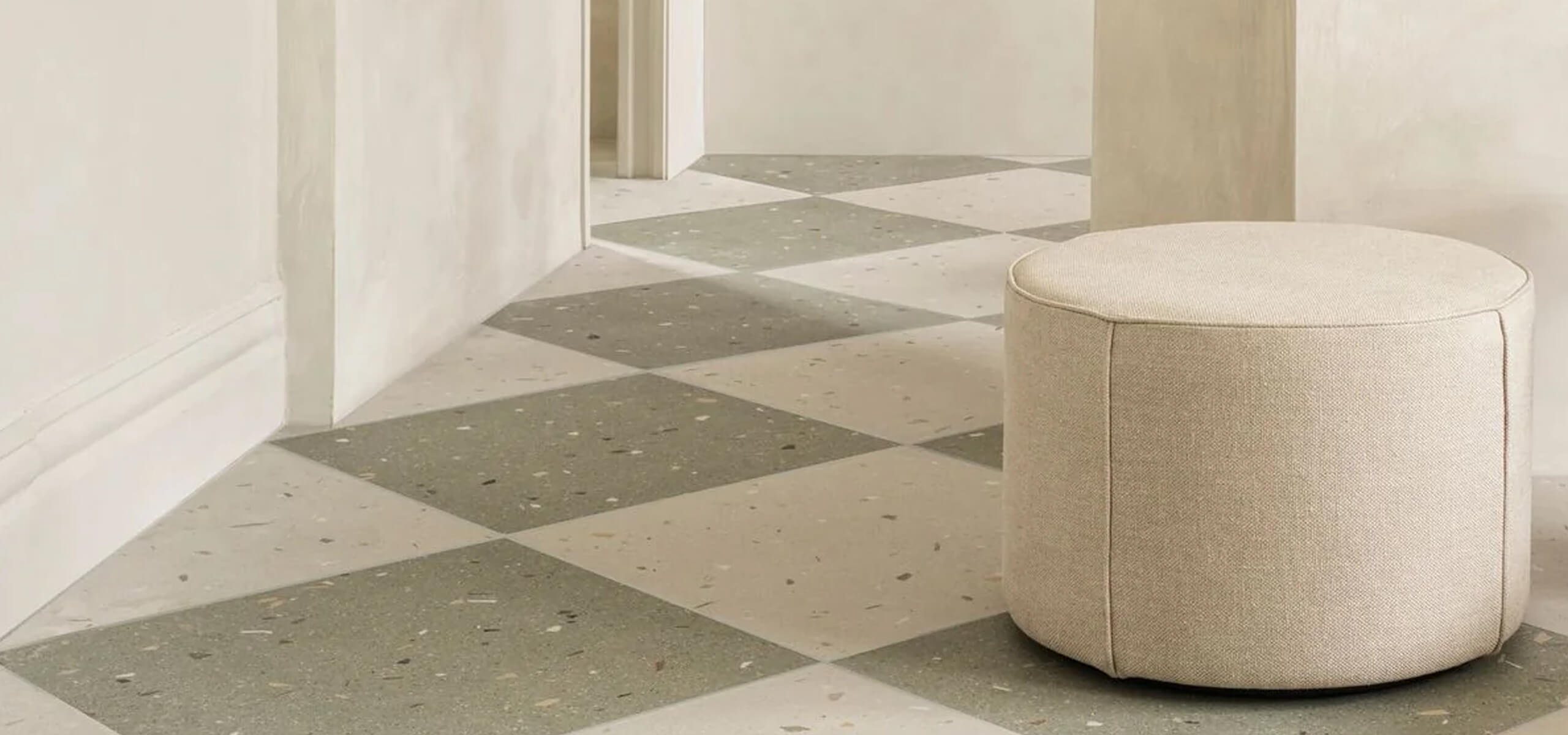 Beige ottoman on a geometric-patterned tiled floor with white walls
