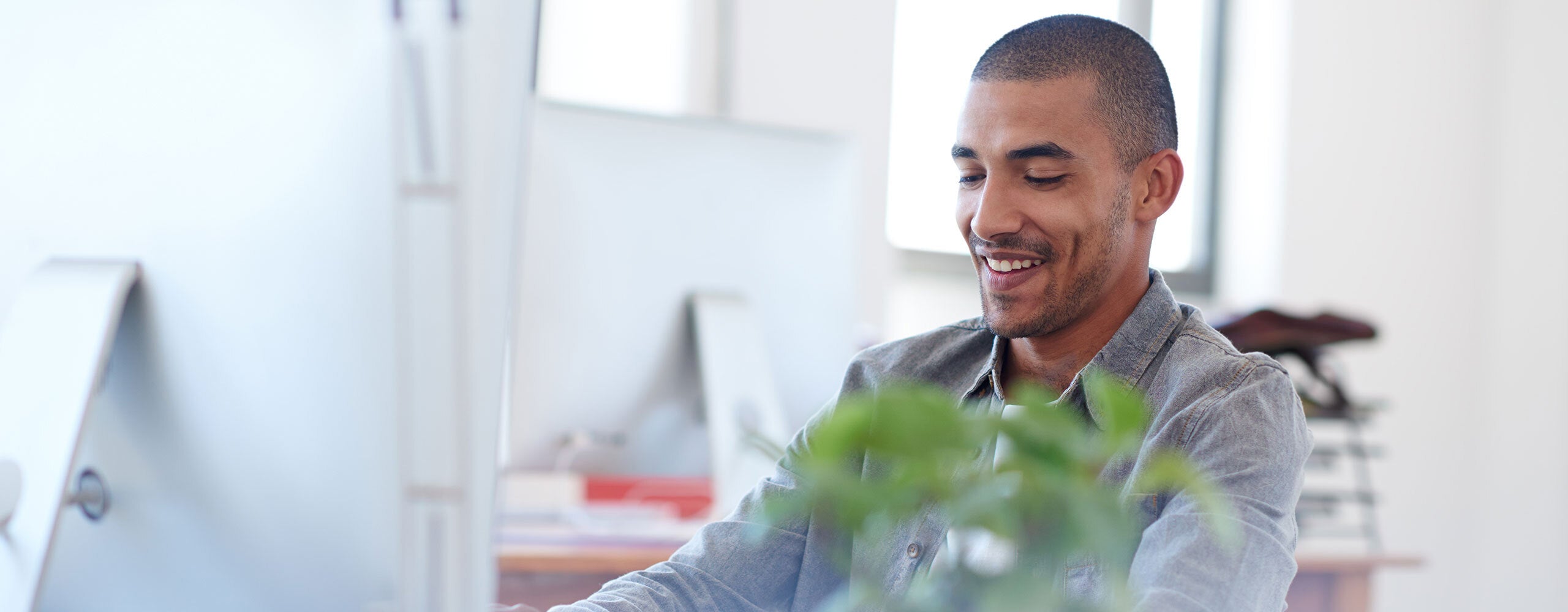 Magento web developer at a desk with a plant, smiling in an ecommerce agency office setting.
