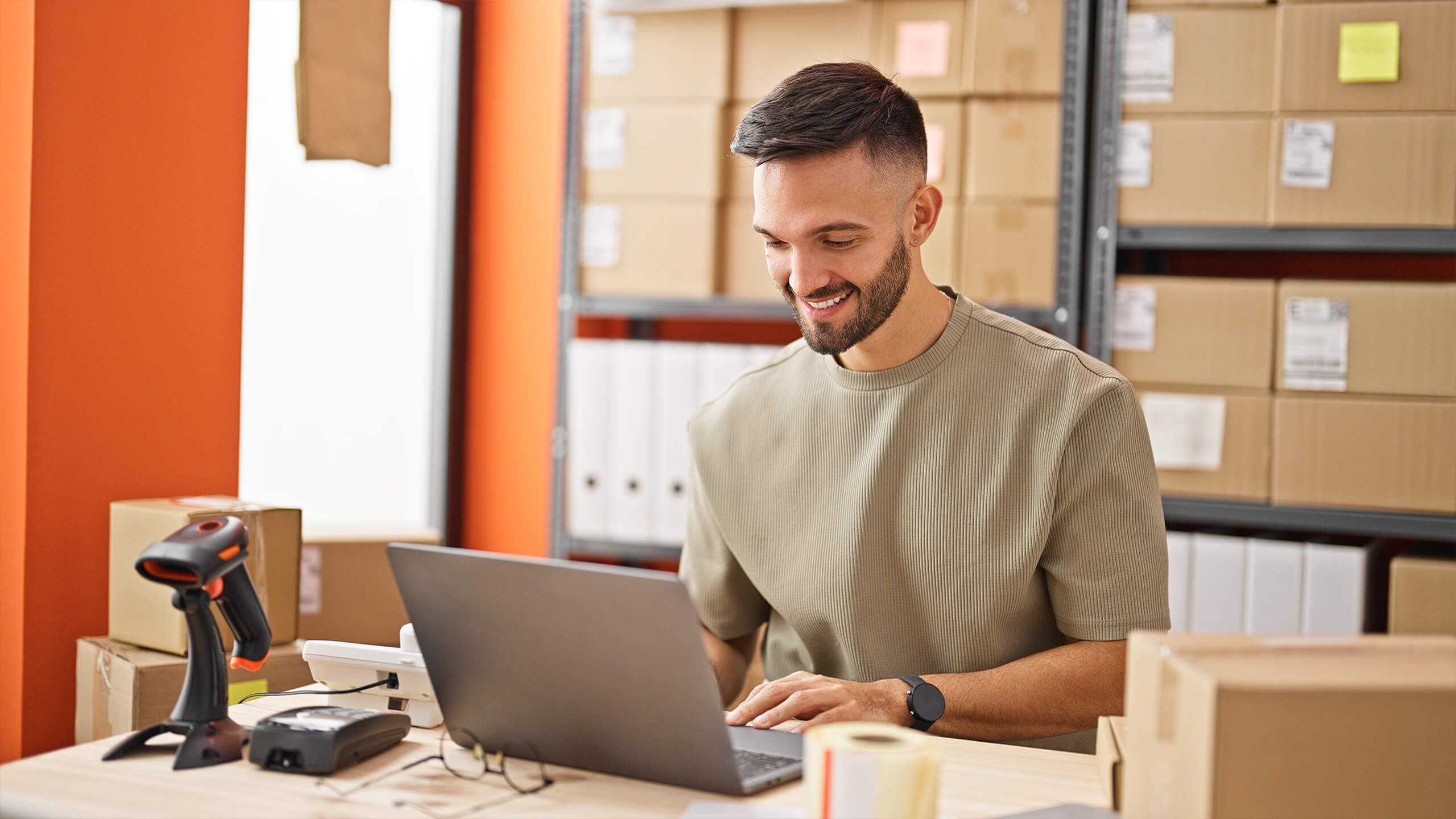 Shopify development services client using a laptop in a warehouse setting with boxes and shelves in the background
